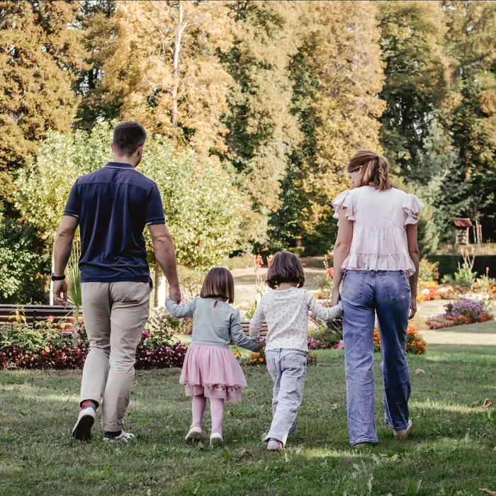 Familie spaziert mit ihren zwei Töchtern Hand in Hand durch einen blühenden Park