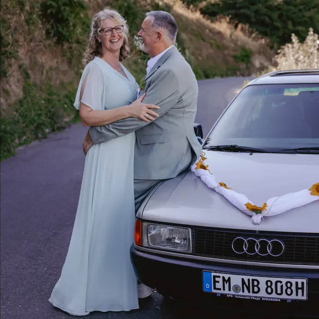 Brautpaar umarmt sich vor dem Hochzeitsauto in den Reben