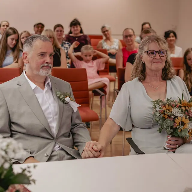 Brautpaar lacht während der Trauung, dahinter die Gäste