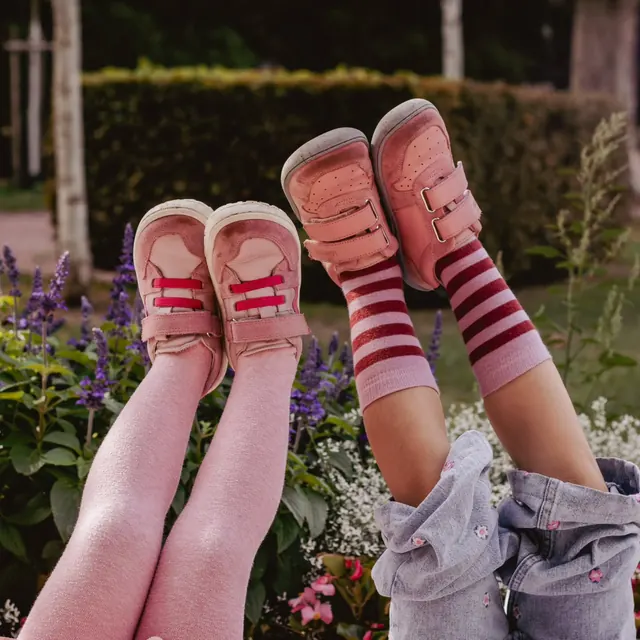 Zwei Kinder strecken lachend die Beine mit rosa Schuhen in die Luft