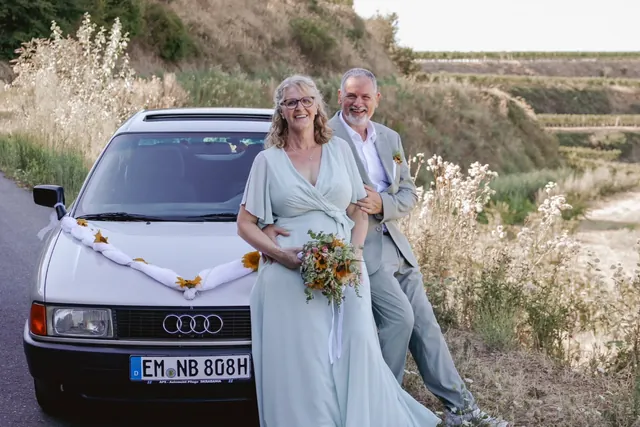 Brautpaar steht am geschmückten Oldtimer in den Weinbergen am Kaiserstuhl